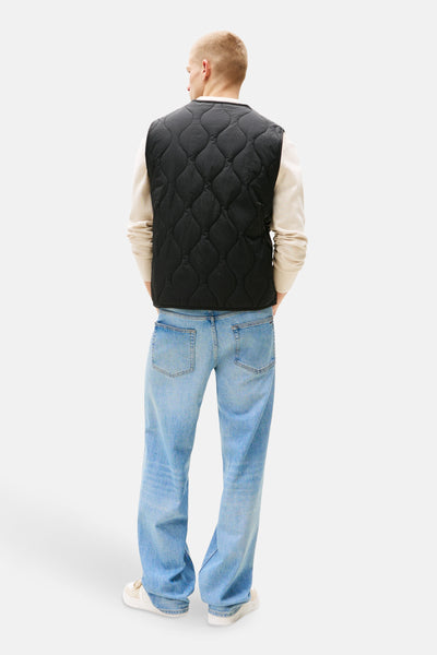 Veste sans manches noire de TOMMY JEANS, matelassée, portée avec un pull et un jean bleu, vue de dos.