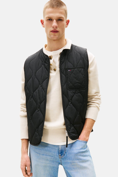 Veste sans manches noire de TOMMY JEANS, matelassée avec poche poitrine et portée sur un pull boutonné et un jean délavé.