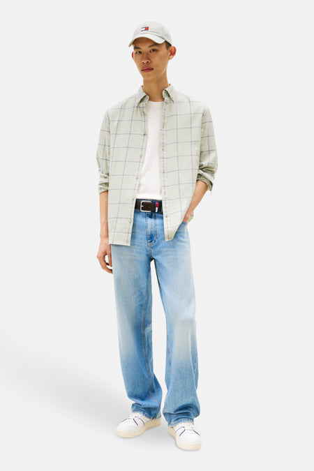 Groen geruit overhemd met lange mouwen van TOMMY JEANS, gedragen open over een wit T-shirt, met een blauwe jeans en een pet.