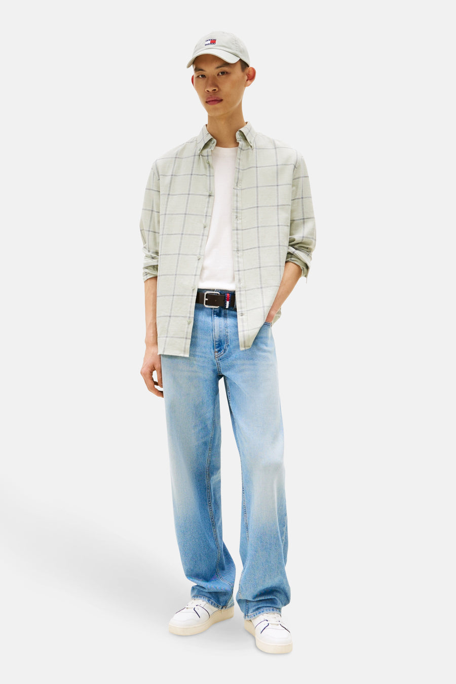 Chemise à manches longues verte à carreaux by TOMMY JEANS, portée ouverte sur un t-shirt blanc, avec un jean bleu et une casquette.