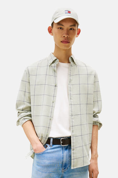 Chemise à manches longues verte à carreaux par TOMMY JEANS, portée ouverte sur un t-shirt blanc, avec un jean bleu et une casquette.