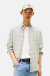 Chemise à manches longues verte à carreaux par TOMMY JEANS, portée ouverte sur un t-shirt blanc, avec un jean bleu et une casquette.