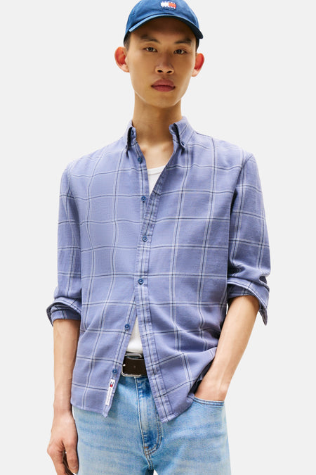 Blauw geruit overhemd met lange mouwen van TOMMY JEANS, gedragen open over een wit T-shirt en een spijkerbroek.