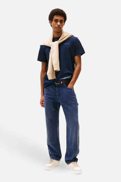 Blauw T-shirt met korte mouwen van TOMMY JEANS, met een beige trui om de nek geknoopt, gedragen met een spijkerbroek en sneakers.