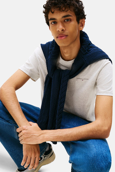 T-shirt à manches courtes gris chiné de TOMMY JEANS, porté avec un pull en maille bleu marine.
