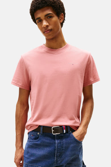 T-shirt rose à manches courtes de TOMMY JEANS, porté avec un jean bleu et une ceinture marron.
