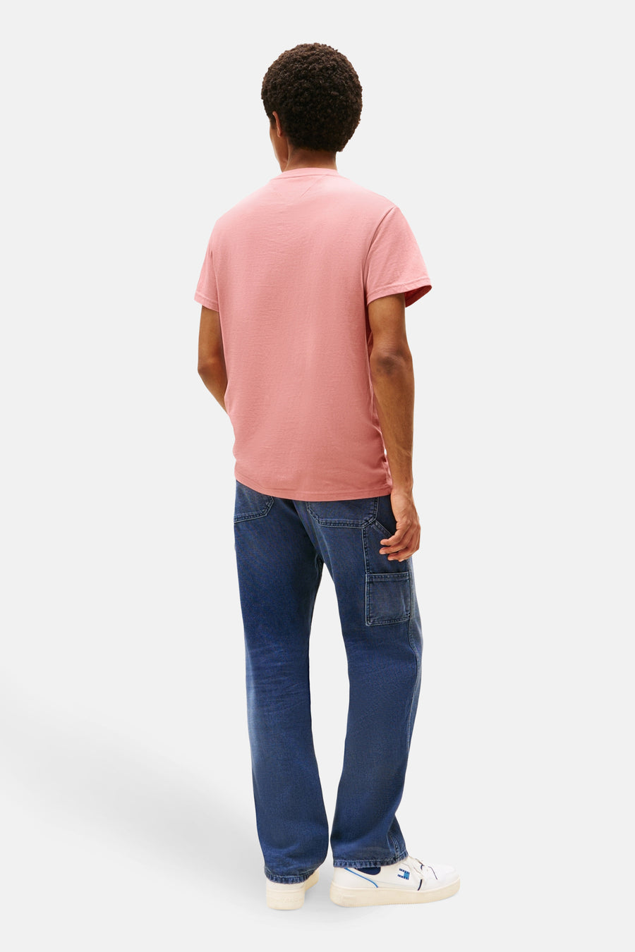 T-shirt à manches courtes rose de TOMMY JEANS, porté avec un jean bleu ample et des baskets blanches.