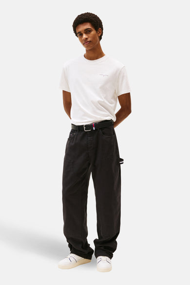 T-shirt à manches courtes blanc de Tommy Jeans, porté avec un pantalon noir ample et des baskets blanches.