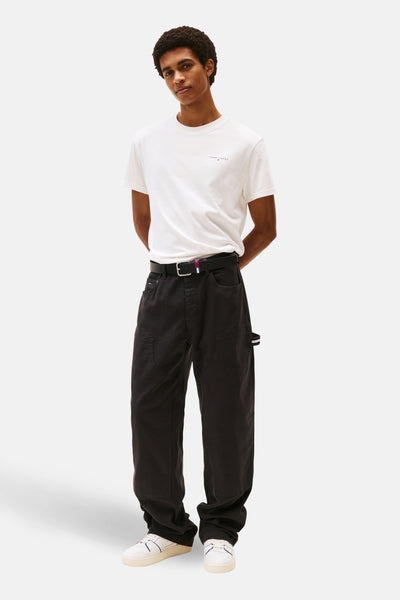 T-shirt à manches courtes blanc de Tommy Jeans, porté avec un pantalon noir ample et des baskets blanches.