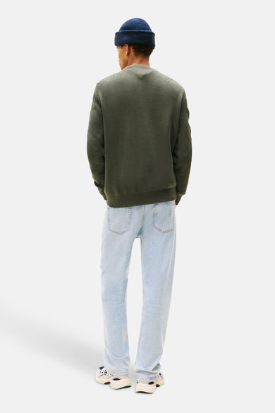 Groene trui met ronde hals van TOMMY JEANS, gedragen met een lichtblauwe jeans en een marineblauwe muts.
