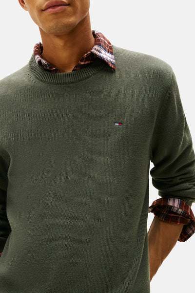 Pull à col rond vert de TOMMY JEANS, porté sur une chemise à carreaux, en maille tricotée.