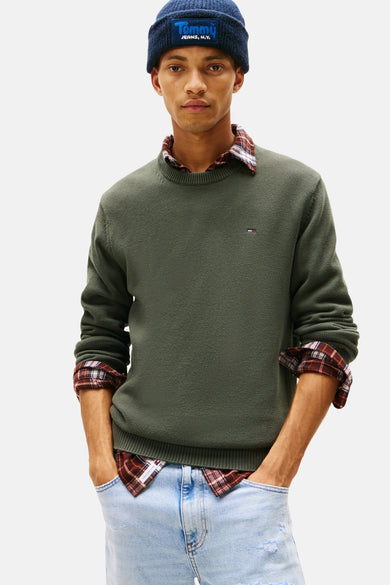 Groene rondehals trui van TOMMY JEANS gedragen over een geruit overhemd, met een donkerblauwe muts.