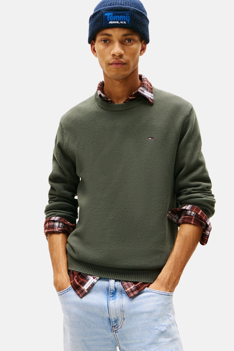 Groene rondehals trui van TOMMY JEANS gedragen over een geruit overhemd, met een donkerblauwe muts.