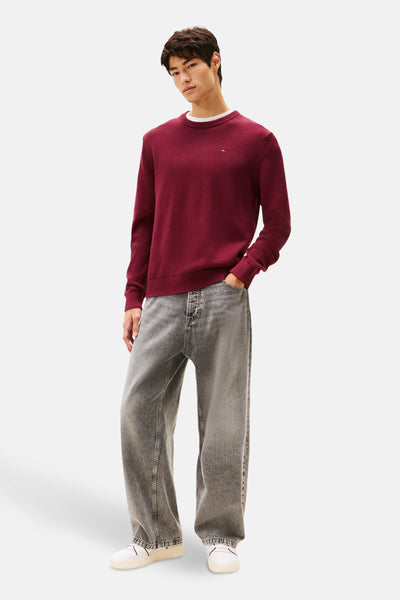 Bordeaux ronde hals trui van TOMMY JEANS, gedragen met een lichtgrijze jeans en witte sneakers.