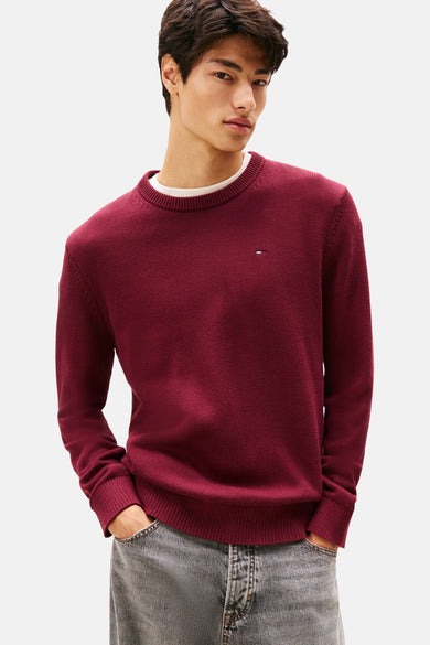 Bordeaux ronde hals trui van TOMMY JEANS, gedragen over een wit T-shirt, met een lichtgrijze jeans.