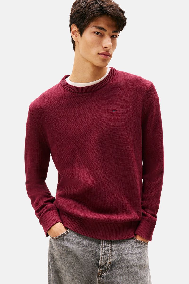 Bordeaux ronde hals trui van TOMMY JEANS, gedragen over een wit T-shirt, met een lichtgrijze jeans.