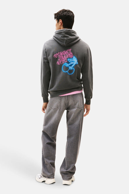 Grijze hoodie van TOMMY JEANS met neonprint op de rug, gedragen met een grijze jeans.