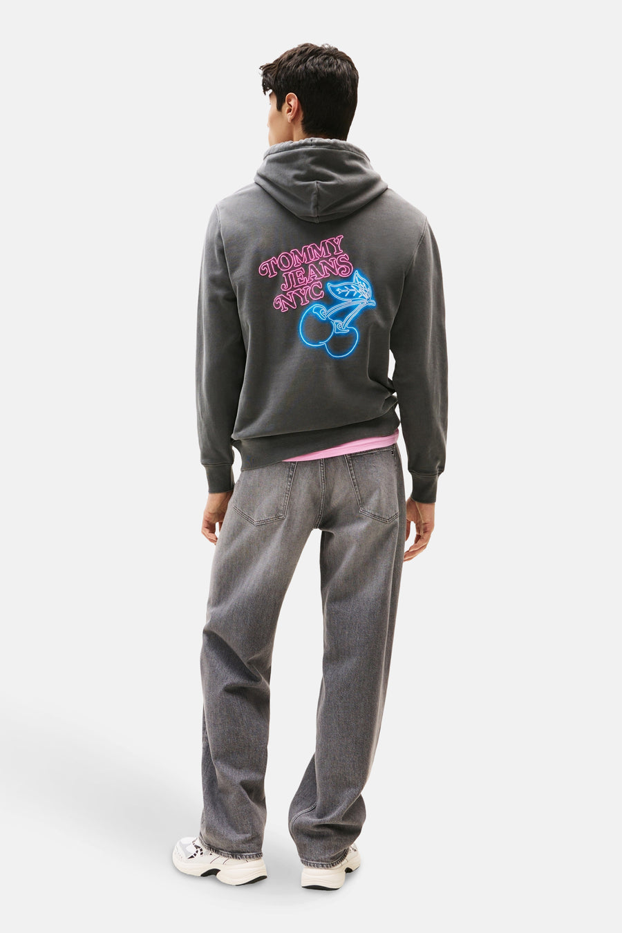 Sweat à capuche gris de TOMMY JEANS avec imprimé néon au dos, porté avec un jean gris.
