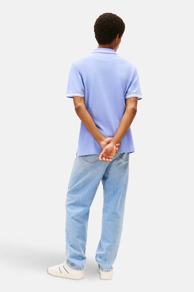 Polo mauve à manches courtes de TOMMY JEANS, porté avec un jean bleu clair et des baskets blanches.