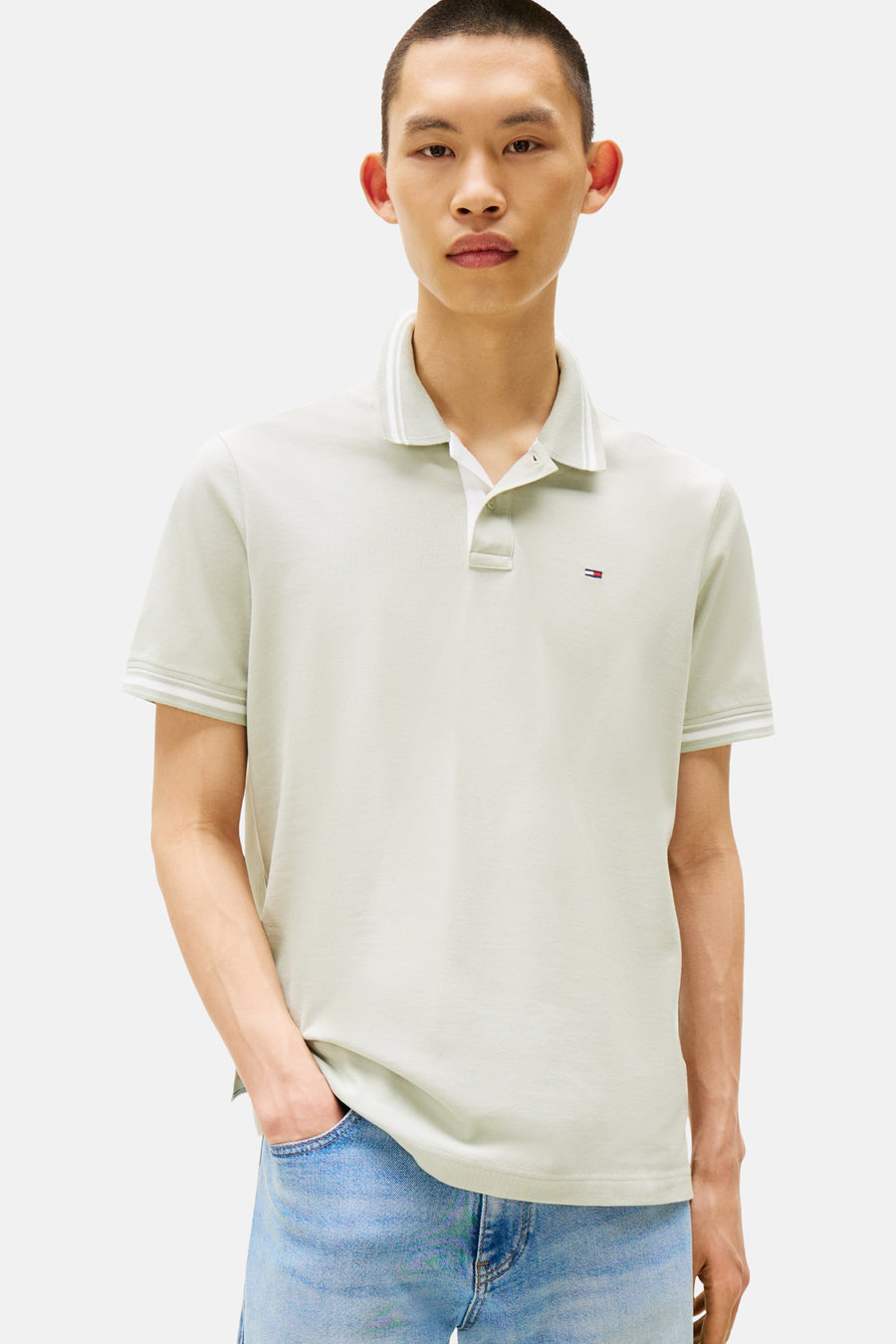 Polo vert clair à manches courtes de Tommy Jeans, avec col et bordures rayés, porté avec un jean bleu.
