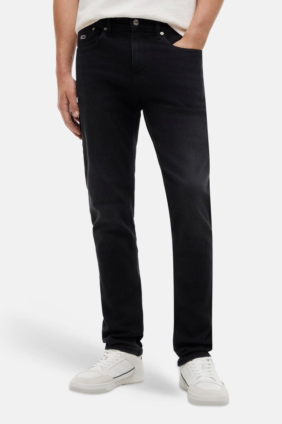 Jeans slim en denim noir de TOMMY JEANS avec une légère décoloration, porté avec des baskets blanches.