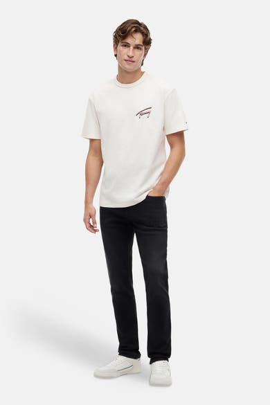 Jeans slim noir en denim de TOMMY JEANS, portés par un homme avec un t-shirt clair et des baskets blanches.