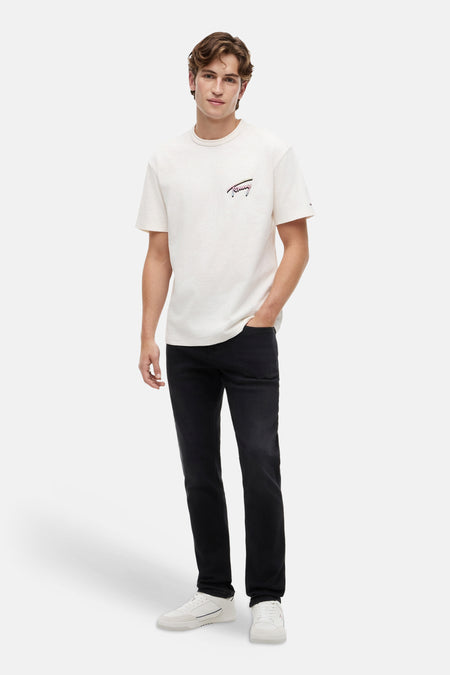 Jeans slim noir en denim de TOMMY JEANS, portés par un homme avec un t-shirt clair et des baskets blanches.