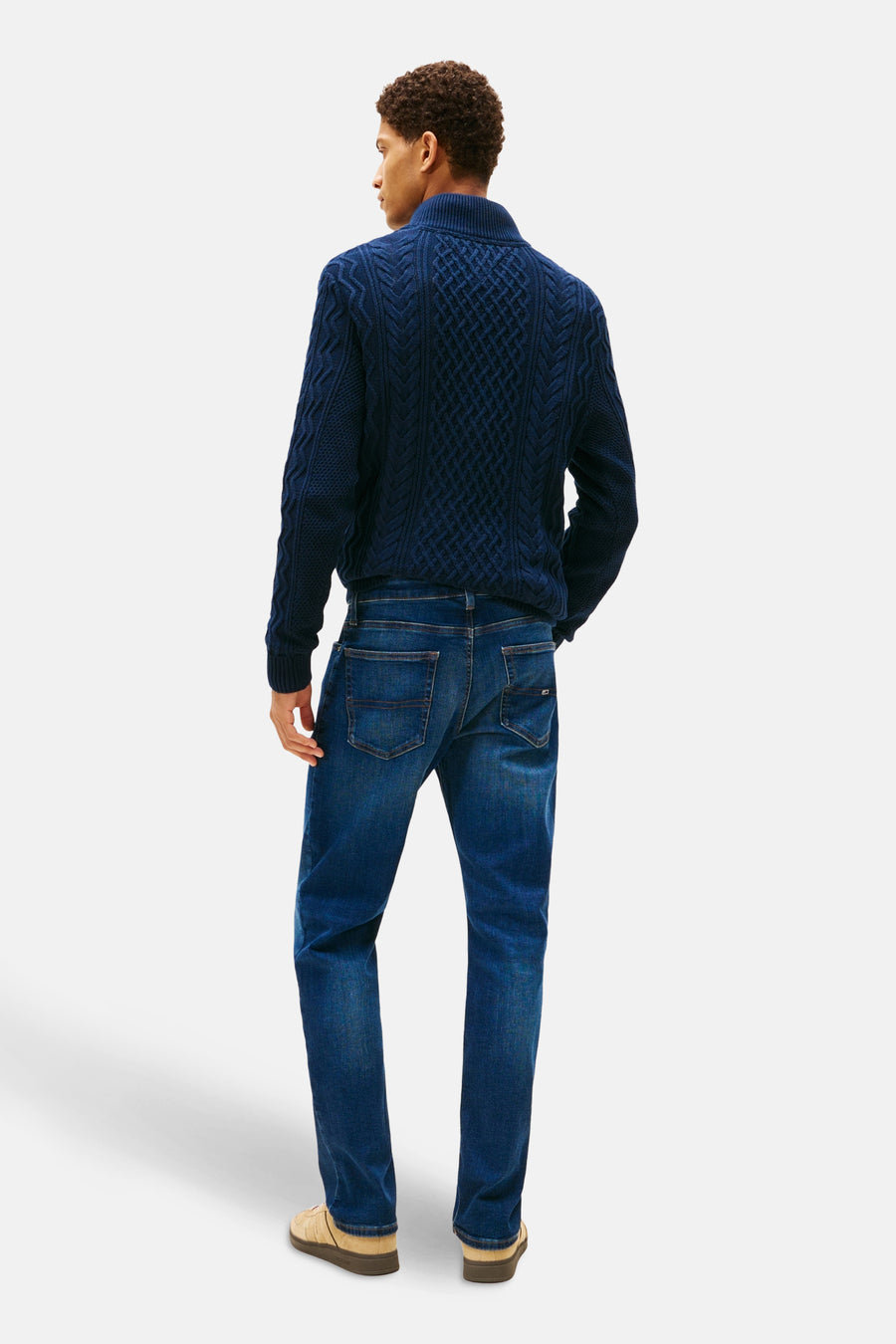 Jean droit en denim bleu foncé de TOMMY JEANS, coupe classique, porté avec un pull en maille torsadée.
