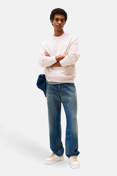 Sweat beige de TOMMY JEANS, porté avec un jean bleu ample et des baskets crème.