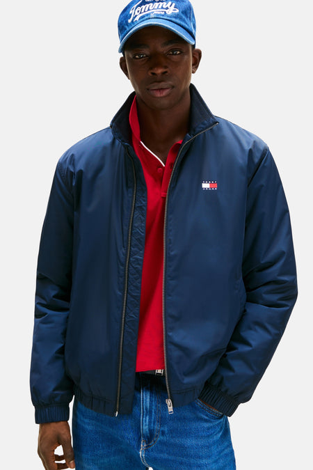Blauwe regenjas van Tommy Jeans, gedragen met een rode polo en een spijkerpet.