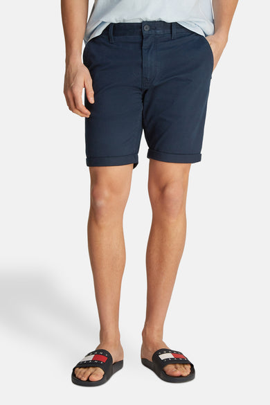 Short bleu de TOMMY JEANS, avec ourlets roulés, porté avec des sandales noires.