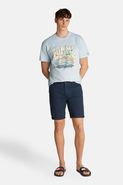 Short bleu de TOMMY JEANS porté avec un t-shirt imprimé et des tongs logotées.