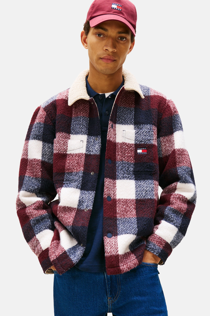 Multikleurig geruit overhemd van TOMMY JEANS, met imitatiebontkraag, gedragen over een blauw poloshirt en een blauwe jeans.