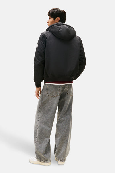 Zwarte regenjas van TOMMY JEANS met capuchon, gedragen met een wijde grijze jeans en witte sneakers.