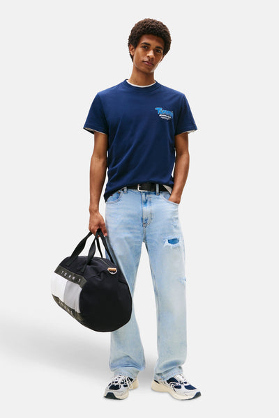 Marineblaues T-Shirt mit kurzen Ärmeln von TOMMY JEANS, mit Logo auf der Brust, getragen mit hellen Jeans und Sportschuhen.