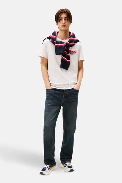 Grijze T-shirt met korte mouwen van TOMMY JEANS, gedragen met een gestreepte trui over de schouders en een blauwe jeans.