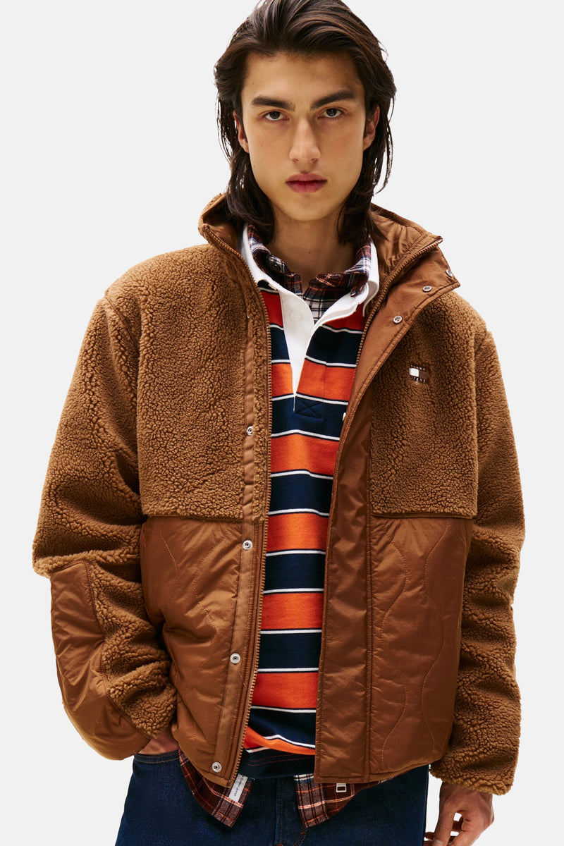 Veste marron effet teddy par TOMMY JEANS avec empiècements matelassés et porté sur un polo rayé et une chemise à carreaux.