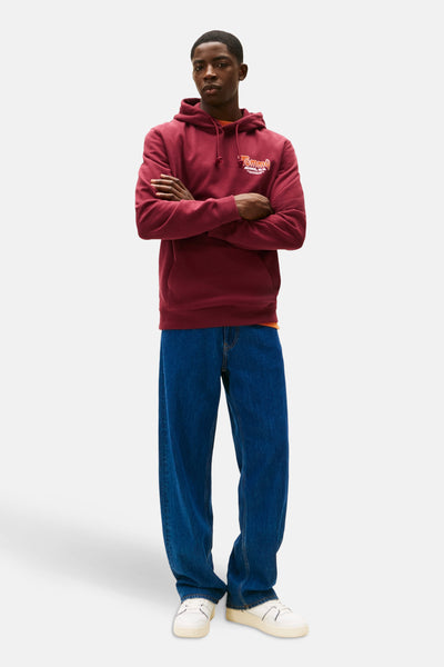 Rode hoodie van TOMMY JEANS, gedragen met een blauwe jeans en witte sneakers.
