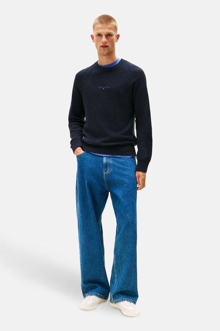 Ronde hals trui van TOMMY JEANS in het blauw met gespikkelde details, gedragen over een blauw T-shirt en een wijde spijkerbroek.