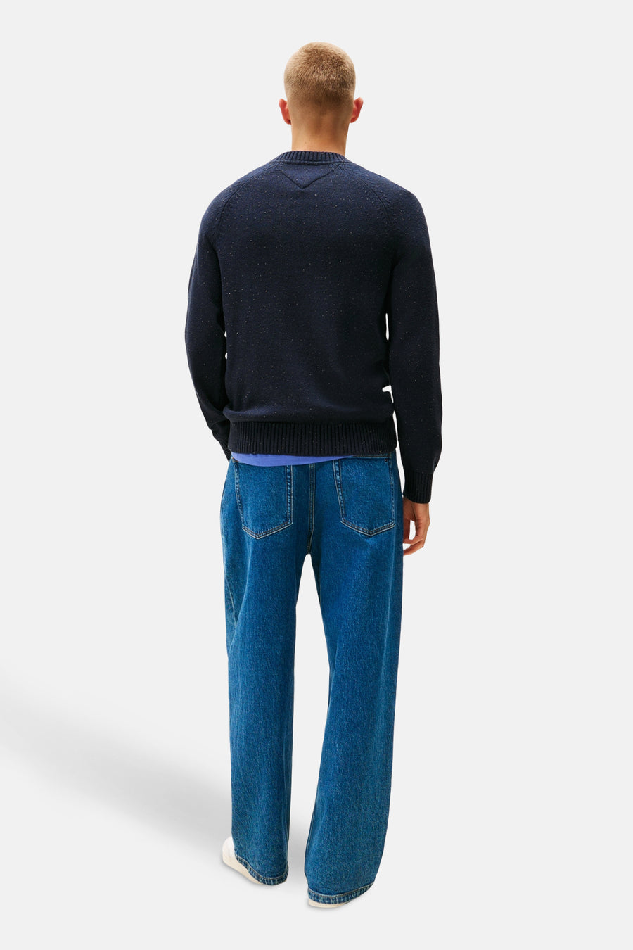 Ronde hals trui blauw van TOMMY JEANS, met gemêleerd patroon, gedragen over een blauw T-shirt en een wijde jeans.