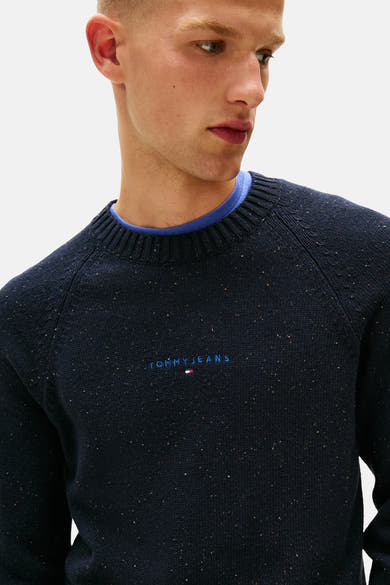 Ronde hals trui van TOMMY JEANS in blauw, gemêleerde breiwerk met geborduurd logo, gedragen over een blauw T-shirt.