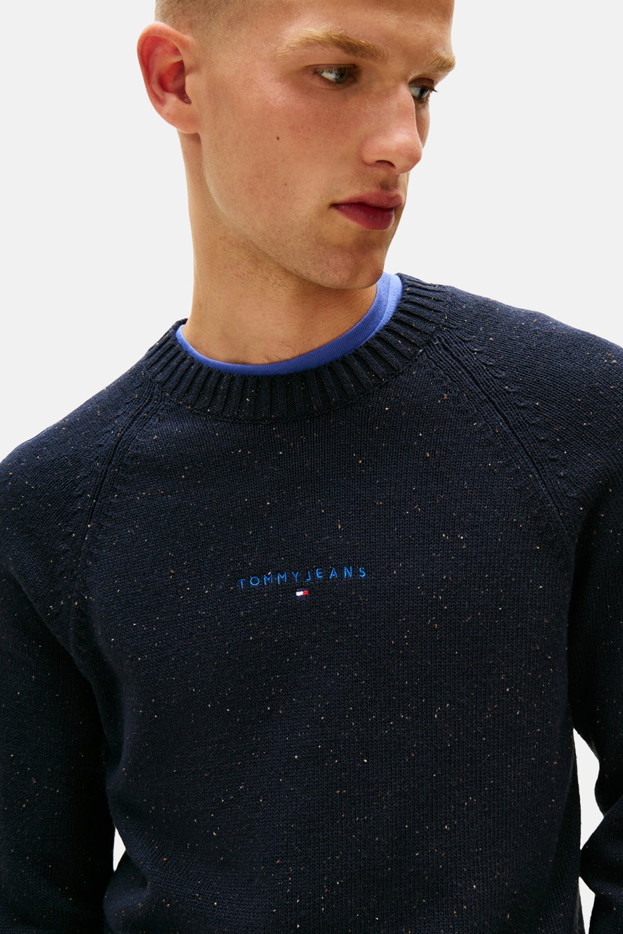 Ronde hals trui van TOMMY JEANS in blauw, gemêleerde breiwerk met geborduurd logo, gedragen over een blauw T-shirt.
