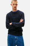 Navyblauwe rondehals-trui van TOMMY JEANS, versierd met kleine spikkels en gedragen over een blauw T-shirt.