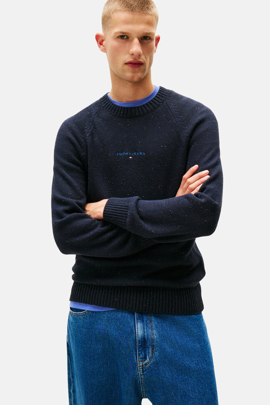 Navyblauwe rondehals-trui van TOMMY JEANS, versierd met kleine spikkels en gedragen over een blauw T-shirt.