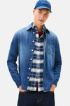 Chemise en jean bleu moyen de TOMMY JEANS, portée ouverte sur une chemise à carreaux et un t-shirt rayé, casquette bleue.