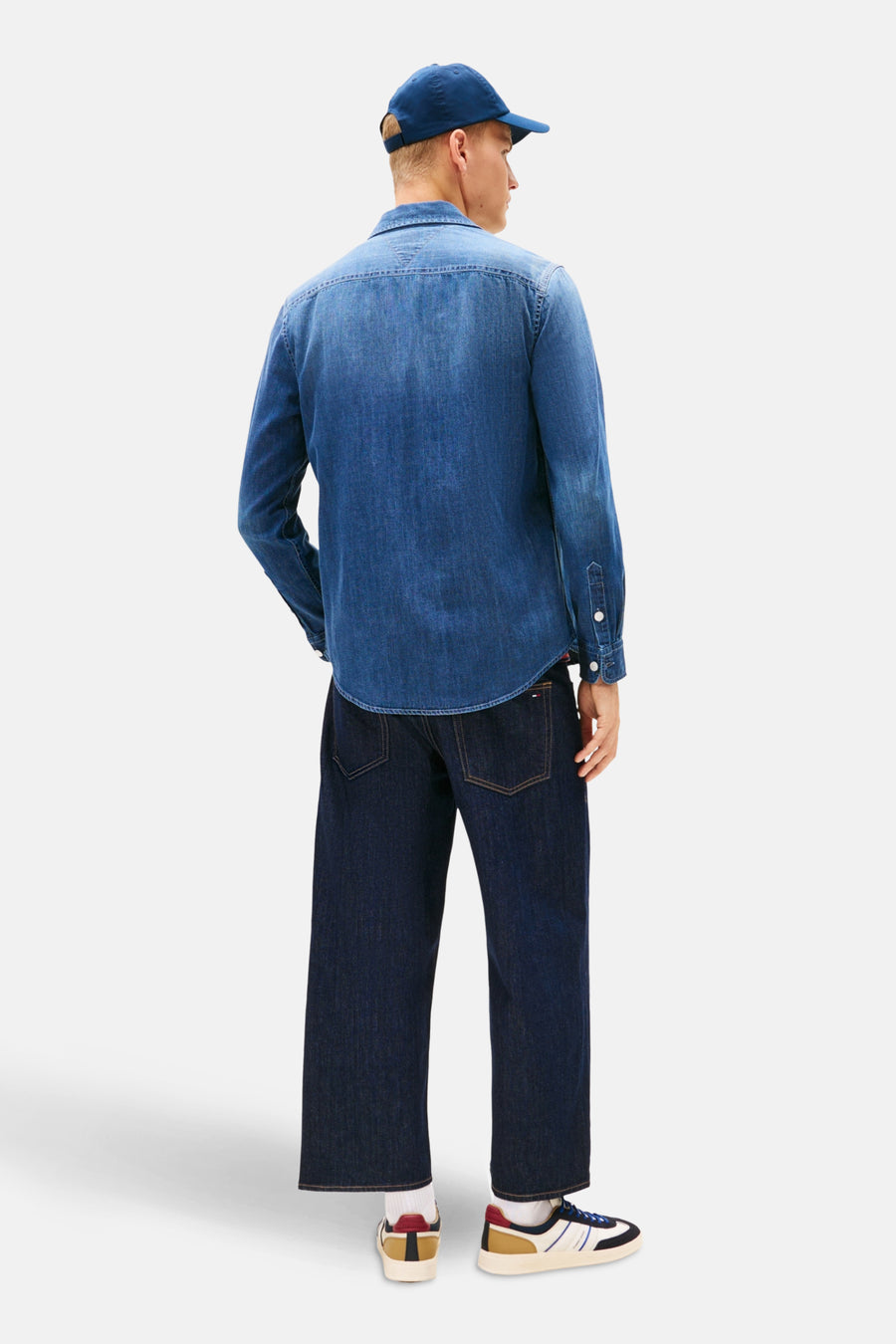 Chemise en jean bleu moyen de Tommy Jeans, vue de dos, portée avec un pantalon et une casquette bleus.