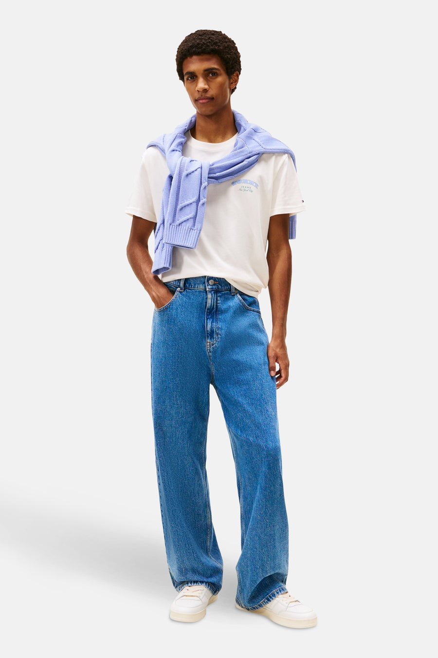 Ecru T-shirt met korte mouwen van TOMMY JEANS, gedragen met een lichtblauwe trui over de schouders en een blauwe jeans