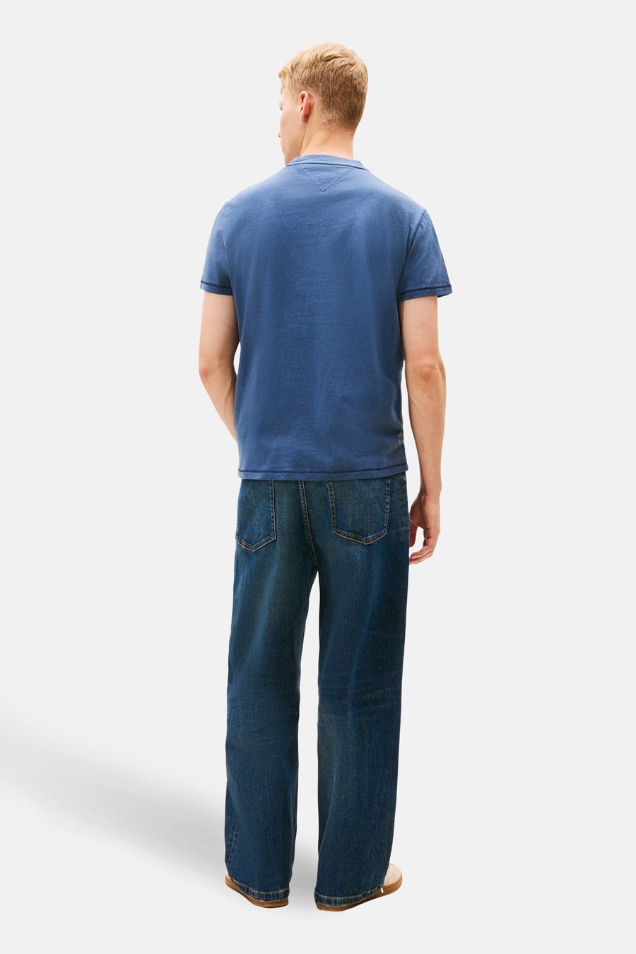 T-shirt à manches courtes bleu de TOMMY JEANS, avec un empiècement triangulaire dans le dos, porté avec un jean ample.