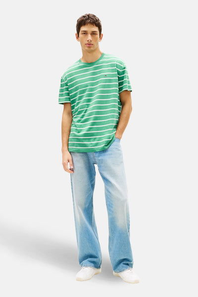 T-shirt à manches courtes vert à rayures blanches de Tommy Jeans, porté avec un jean bleu ample et des baskets blanches.