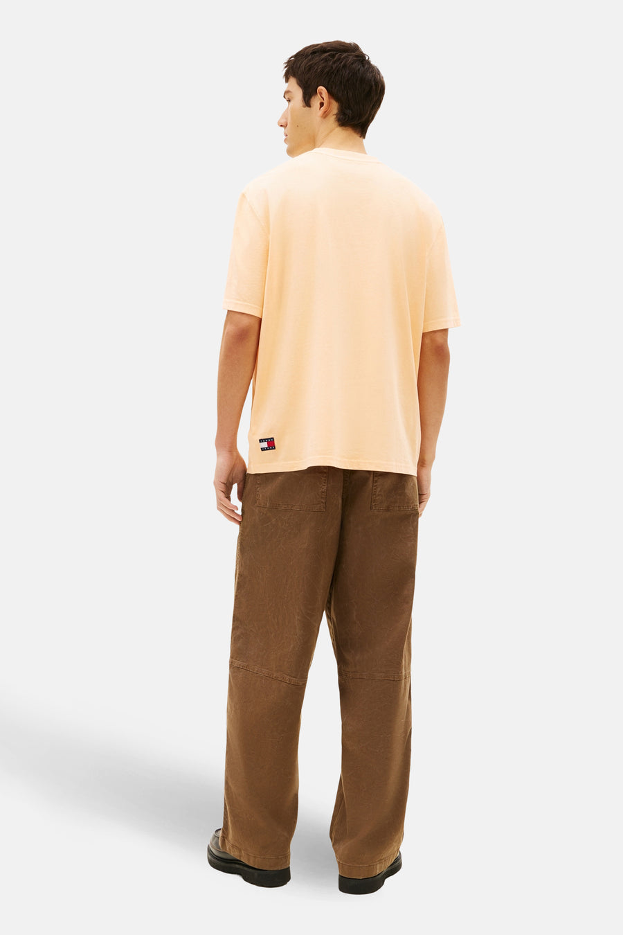 T-shirt orange à manches courtes de TOMMY JEANS, avec un logo carré sur le côté, porté avec un pantalon marron.